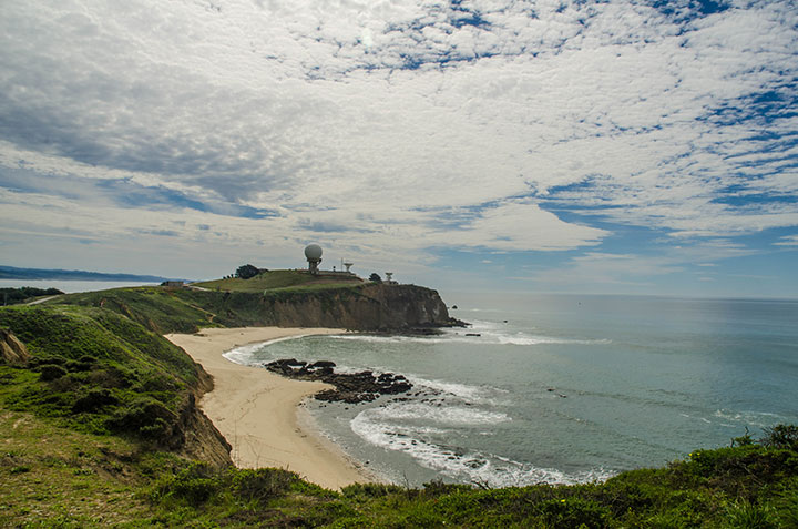 a narrow, grassy plateau lined with sandy beach extending into the ocean